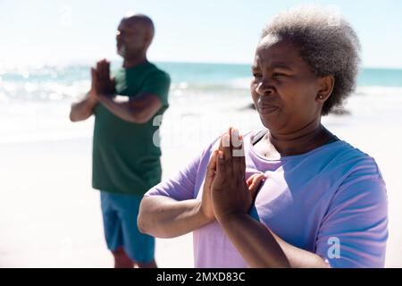 afroamerikanisches Seniorenpaar meditiert im Sommer am Strand vor klarem Himmel Stockfoto