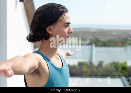 Ein glücklicher birassistischer Mann, der Yoga macht, sich auf dem Balkon streckt Stockfoto