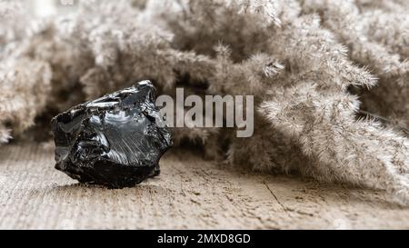 Rohes, ungeschliffenes, schwarzes Opalstein auf Holzhintergrund. Schwarzes Opal ist ein seltenes und teures Schmuckstück Stockfoto