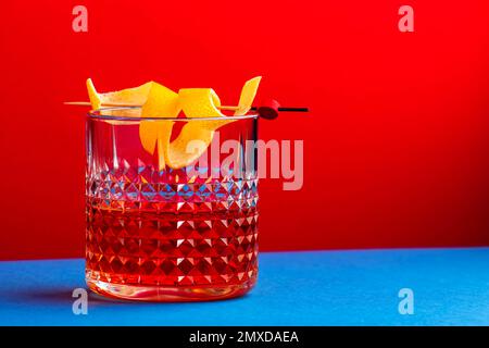 Sazerac-Cocktail mit Cognac, Bourbon, Absinth, Bitter, Zucker und Zitronenschale. Glitzernder rot-blauer Hintergrund mit hartem Licht Stockfoto