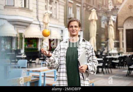 Frau, die auf der Straße unterwegs ist und ein Notebook in der Hand hält und Frau, die mit Orange jongliert, Stadtleben. Stockfoto