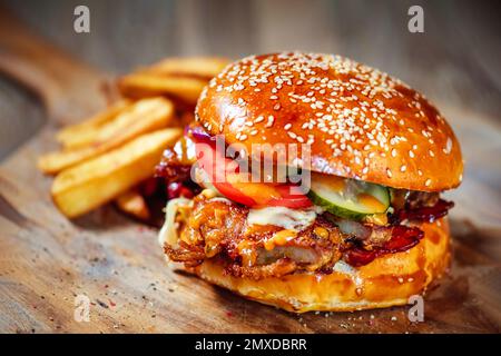Saftiger Burger mit Schweinerippchen, scharfer Sauce und frischem Gemüse auf Holzbrett Stockfoto