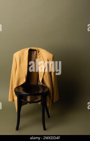 Modischer gelber Blazer auf schwarzem Holzstuhl auf olivgrünem Hintergrund, Stockbild Stockfoto
