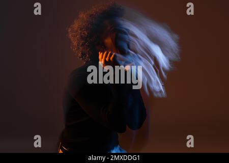 Bewegungsunschärfe eines jungen afroamerikanischen Mannes mit bipolarer Störung auf dunklem Hintergrund mit orangefarbenem und blauem Licht, Stockbild Stockfoto