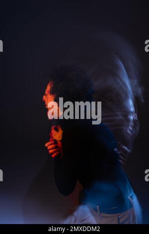 Doppelte Belichtung von verwundeten und wütenden afroamerikanischen Männern, die auf schwarzem Hintergrund mit rotem und blauem Licht schreien, Stockbild Stockfoto