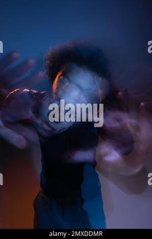 Doppelbelichtung eines verwundeten afroamerikanischen Mannes mit bipolarer Störung, der im Dunkeln auf die Kamera blickt, mit orangefarbenem und blauem Licht, Stockbild Stockfoto
