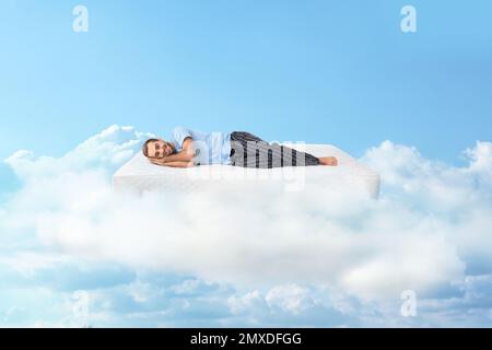 Junger Mann, der auf einer Matratze in Wolken liegt Stockfoto