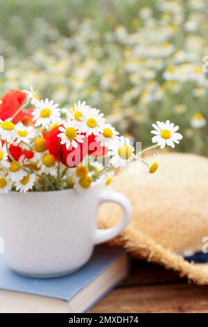 Becher mit Kamillen und Mohn auf Holztisch im Freien Stockfoto