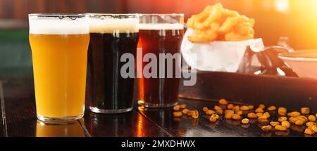 Gläser leckeres Bier und Snacks auf einem Holztisch in der Bar. Bannerdesign Stockfoto