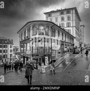 Eine Graustufenaufnahme des Cuppins-Gebäudes an einem Regentag mit Leuten, die in Lausanne herumlaufen Stockfoto