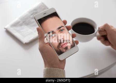 Mann mit Smartphone und Gesichtserkennungssystem am Tisch, Nahaufnahme. Biometrische Verifizierung Stockfoto