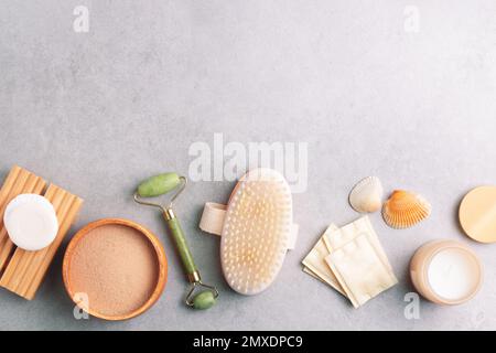 Set aus Hautpflegeprodukten und Wellnessprodukten. Massagebürste, Jadewalze, Wattepads, Seife, Gesichtsmaske aus Ton auf grauem Steinhintergrund. Stockfoto
