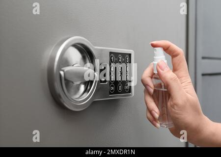 Frau, die Antiseptikum auf die Tastatur des modernen Safes sprüht, Nahaufnahme Stockfoto