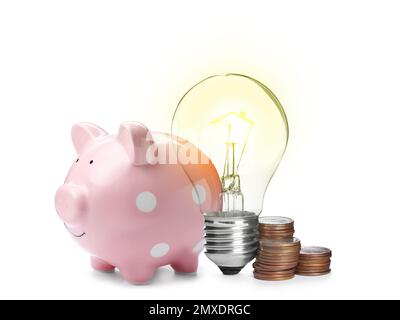 Glühbirne mit Wolfram-Filament auf dem Hausdach, Sparschwein und Münzen auf weißem Hintergrund. Energieeffizienz, Darlehen, Immobilien oder Geschäftsidee Stockfoto