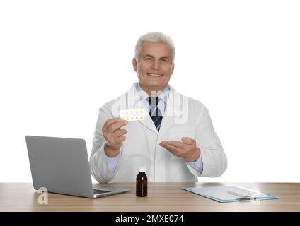 Professioneller Apotheker mit Pillen und Laptop am Tisch vor weißem Hintergrund Stockfoto