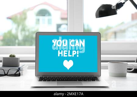 Das Spendenkonzept. Laptop mit Text, DEN SIE am Tisch im Büro AUSHELFEN können Stockfoto