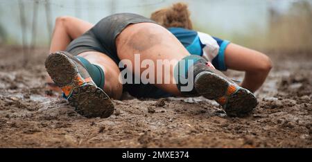 Schlammläufer. Kriechend, vorbei an Hindernissen mit Stacheldraht bei extremen Hindernisrennen Stockfoto