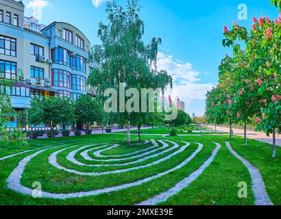 Der Park am Ufer von Obolonska mit Birkenbäumen, blühenden roten Rosskastanien und dem Labyrinth auf dem Rasen, Kiew, Ukraine Stockfoto
