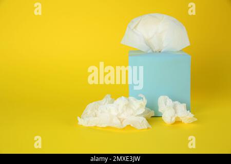 Gebrauchte Papiertücher und Schachtel auf gelbem Hintergrund. Platz für Text Stockfoto