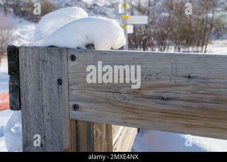 Schneebedeckter Holzzaun an der Seite einer Skipiste mit den Worten „Bonne Journee“ über einem lächelnden Gesicht. Stockfoto