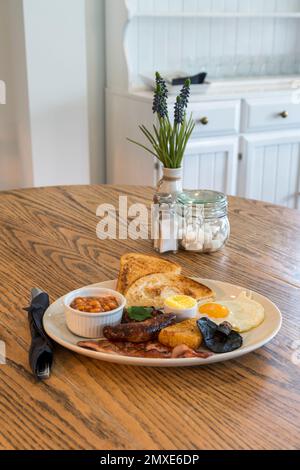 Innenaufnahmen eines hellen und luftigen Cafés mit Holztisch. Komplettes englisches Frühstück auf dem Tisch - aus der Sicht Stockfoto