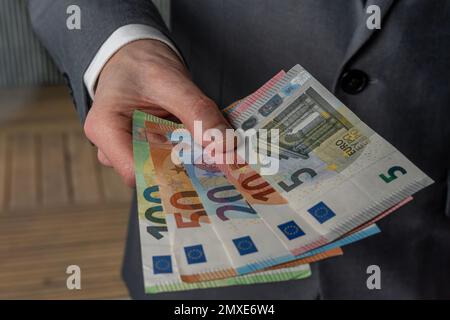 Stillleben. Ein Mann in einem Geschäftsanzug hält fließende Euro-Banknoten unterschiedlicher Werte in der Hand Stockfoto