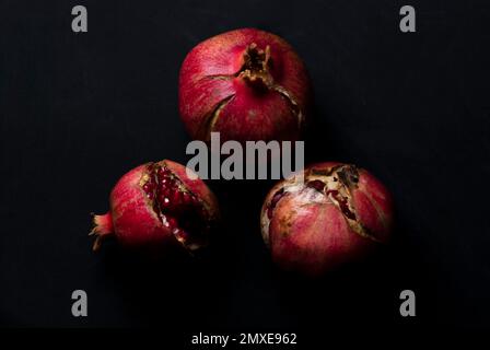 Offene rote reife Granatäpfel, bereit zum Essen auf schwarzem Hintergrund, Blick von oben Stockfoto