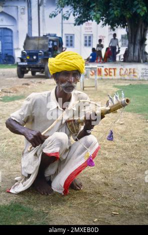 Historisches Archivbild eines Rajashtani-Straßenmusikers in farbenfrohem Turban-Squatting, der ein antikes, gebogenes Folk Instrument oder Ravanahatha spielt, Vorfahren der Violin in Pushkar India 1990 Stockfoto