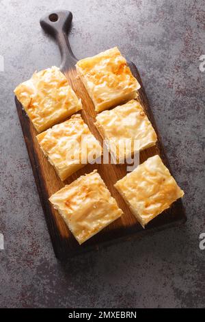 Galaktoboureko ist ein traditionelles griechisches Dessert mit einem Vanillesauce in knusprigem Phyllo-Gebäck auf dem Holzbrett auf dem Tisch. Vertikale Draufsicht Stockfoto