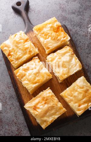 Galaktoboureko ist ein griechisches, türkisches, lazesisches und syrisches Dessert aus Grieß-Vanillesauce, gebacken in Filo-Nahaufnahme auf dem Holzbrett auf dem Tisch. Vertikal oben V Stockfoto