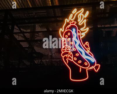 Neon Hot Dog Schild in der Hand feurig, Street Food, Besucherattraktion, rot-orange feurige Farbe, leuchtet im Dunkeln, an der Wand eines Food Court Rest Stockfoto