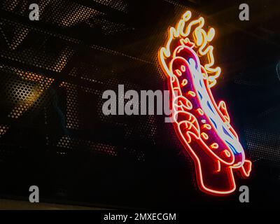 Neon Hot Dog Schild in der Hand feurig, Street Food, Besucherattraktion, rot-orange feurige Farbe, leuchtet im Dunkeln, an der Wand eines Food Court Rest Stockfoto