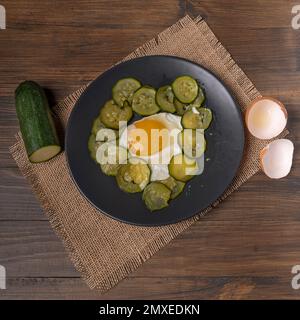 Draufsicht auf einen Teller mit Spiegelei und Zucchini auf einem Jute-Tischset Stockfoto
