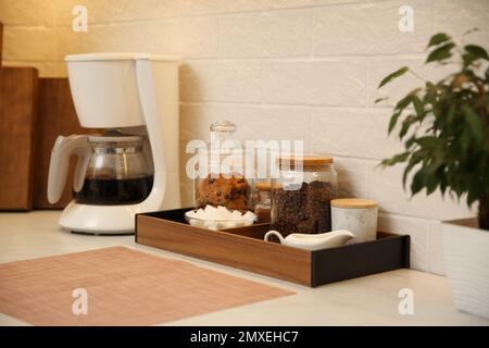 Moderne Kaffeemaschine auf der Arbeitsfläche nahe der weißen Backsteinwand in der Küche Stockfoto