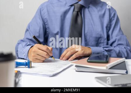 Geschäftsmann, der die Dokumentdaten prüft, die Steuerfinanzierung und den Papierkram übernimmt oder Rechtsinformationen liest. Geschäftsbericht mit Vertragsunterzeichnung am Schreibtisch. Stockfoto