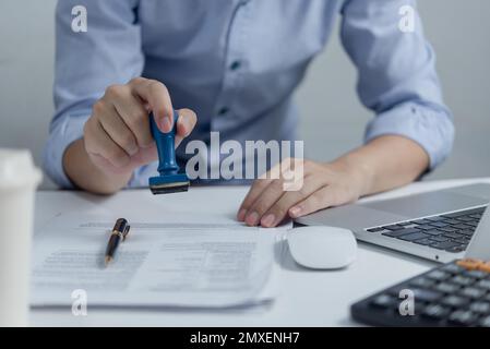 Mann, der die Genehmigung von Dokumenten für das Bankwesen oder das Investment-Marketing auf dem Schreibtisch stempelt. Stockfoto