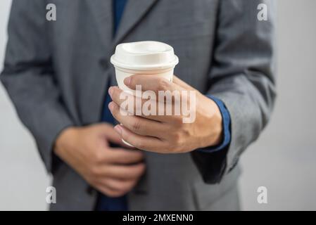 Ein Geschäftsmann, der eine Kaffeetasse aus weißem Papier zum Mitnehmen hält. Stockfoto