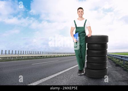 Mechaniker in Uniform mit Autoreifen auf Asphaltstraßen im Freien, Platz für Text Stockfoto