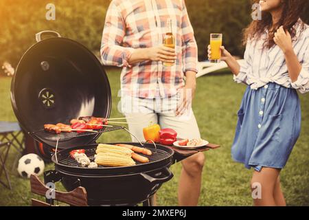 Leute mit Getränken in der Nähe des Grills draußen an sonnigen Tagen Stockfoto