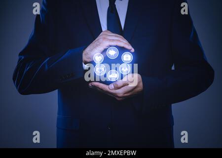 Geschäftsmann mit verschiedenen Symbolen auf dunklem Hintergrund, Nahaufnahme. Versicherungskonzept Stockfoto