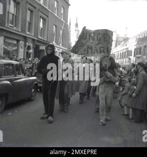 1955, historisch, Studentenwoche, junge Männer laufen in einer Prozession entlang einer High Street, Cambridge, England, Großbritannien, beobachtet von Einheimischen. Angeführt von zwei jungen Männern in Gorilla- und Löwenkostüm, die ein Banner mit der Aufschrift „Hungermarsch“ in der Hand halten. Stockfoto