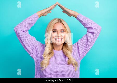 Foto von einem strahlenden Zahnlächeln blonde maklerin mittleren Alters zeigt ein Symbol für die Handsicherheit isoliert auf aquamarinfarbenem Hintergrund Stockfoto