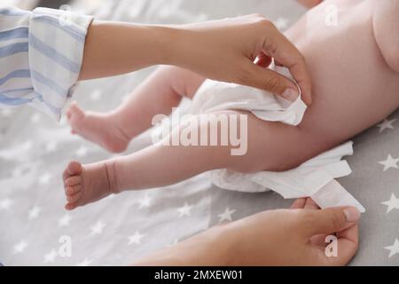 Mutter wechselt die Windel ihres Babys auf dem Bett und schließt Stockfoto