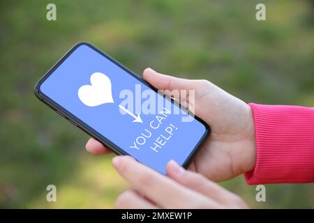 Das Spendenkonzept. Frau, die ihr Smartphone mit SMS hält, DIE IHR draußen UND Nahaufnahmen MACHEN KÖNNT Stockfoto