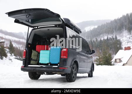 Schwarzes Auto mit Gepäck im Kofferraum auf verschneiter Straße. Winterurlaub Stockfoto