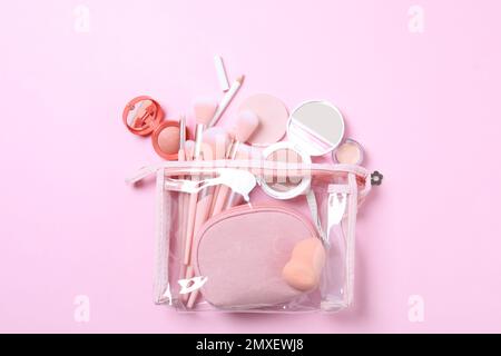 Kosmetiktasche aus Kunststoff mit Make-up-Produkten und Kosmetikartikeln auf pinkfarbenem Hintergrund, flach gelegt Stockfoto