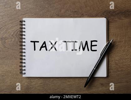 Notizbuch mit Worten TAX TIME und Stift auf Holztisch, Draufsicht Stockfoto