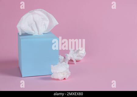 Karton mit Papiertüchern und gebrauchten zerknitterten Servietten auf rosafarbenem Hintergrund, Platz für Text Stockfoto