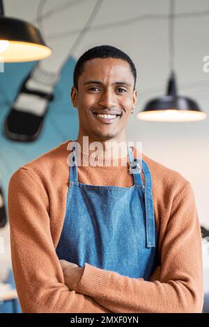 Lächelnder Eigentümer oder Kellner in Arbeitskleidung steht in einer modernen Cafeteria oder einem Restaurant-Pub - Konzept der Jobsuche - Arbeiten im Catering - vertikales Porträt Stockfoto