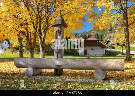 Der herrlichen Brunnen aus einem Baumstamm im Vordergrund auf dem Dorfplatz von Aaufham mit der Kirche St. Jakobus im Hintergrund, GMD. Wut, Beschr Stockfoto